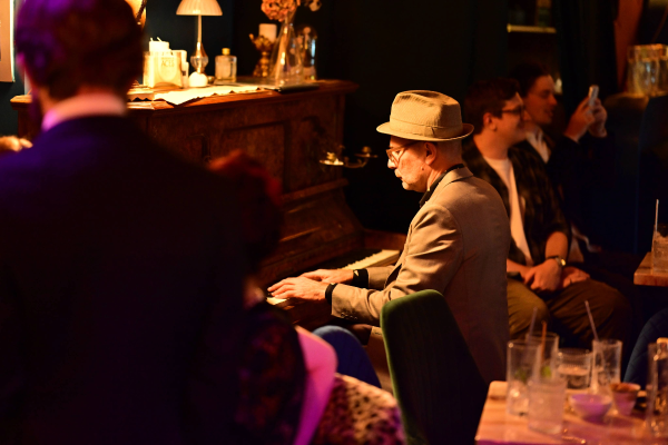 Man playing piano at Aces Bar in Brunswick Aces Distillery in a dimly lit room with other people around