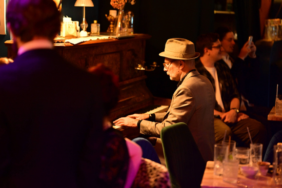 Man playing piano at Aces Bar in Brunswick Aces Distillery in a dimly lit room with other people around